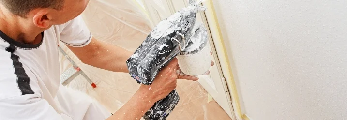 Person streicht Wand mit Farbspritzpistole